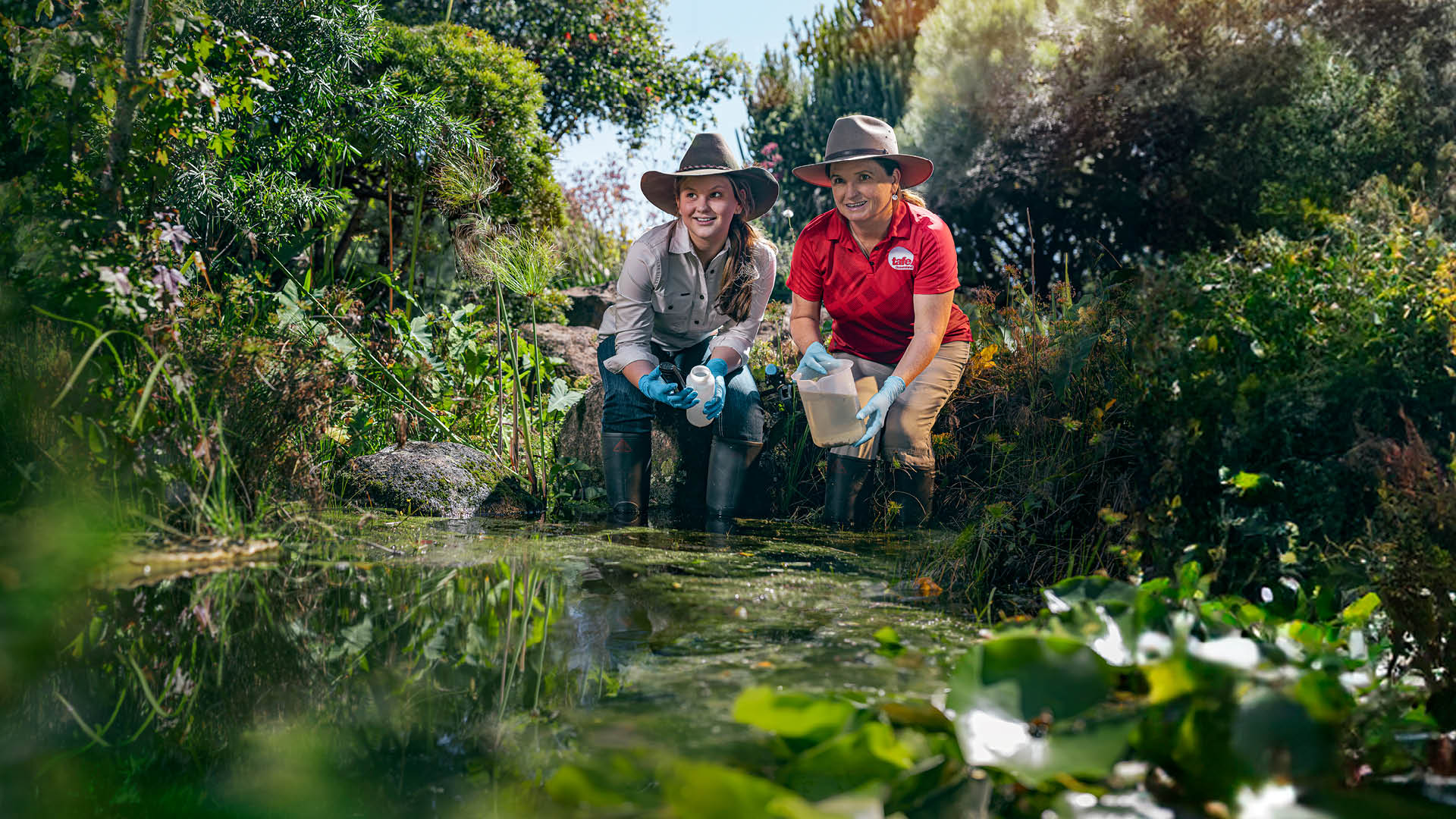 student and teacher feeding fish in pond