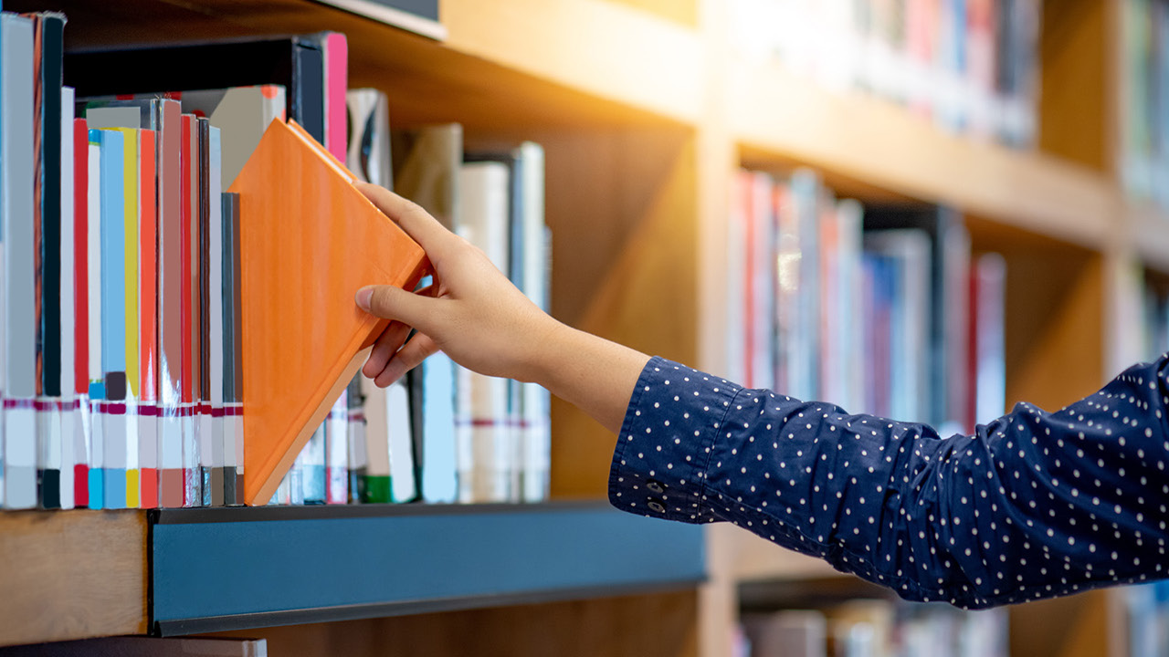 Photograph of a person grabbing a book in a library
