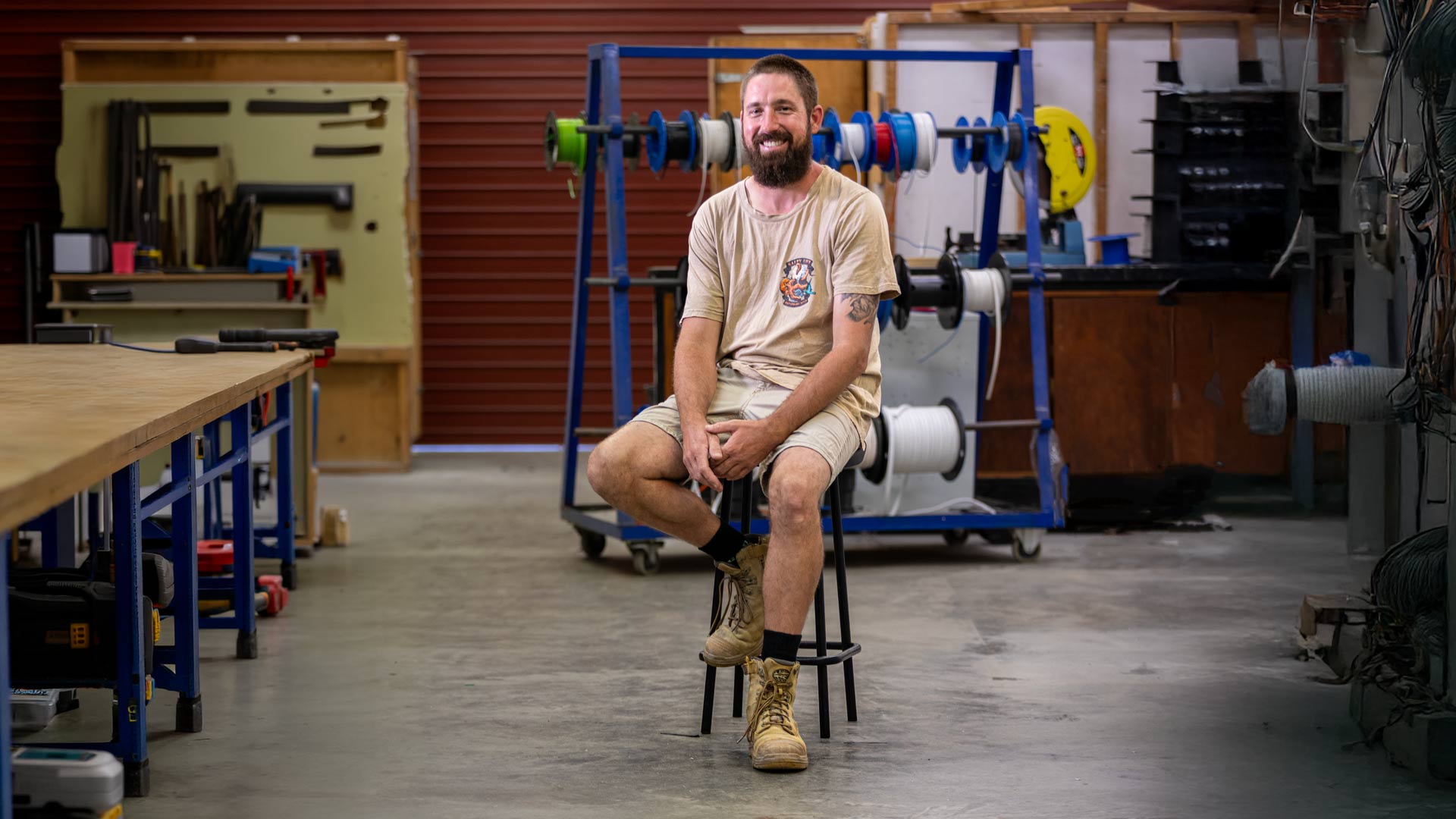 Christpoher looking at camera sitting on chair with campus electrical workshop in background